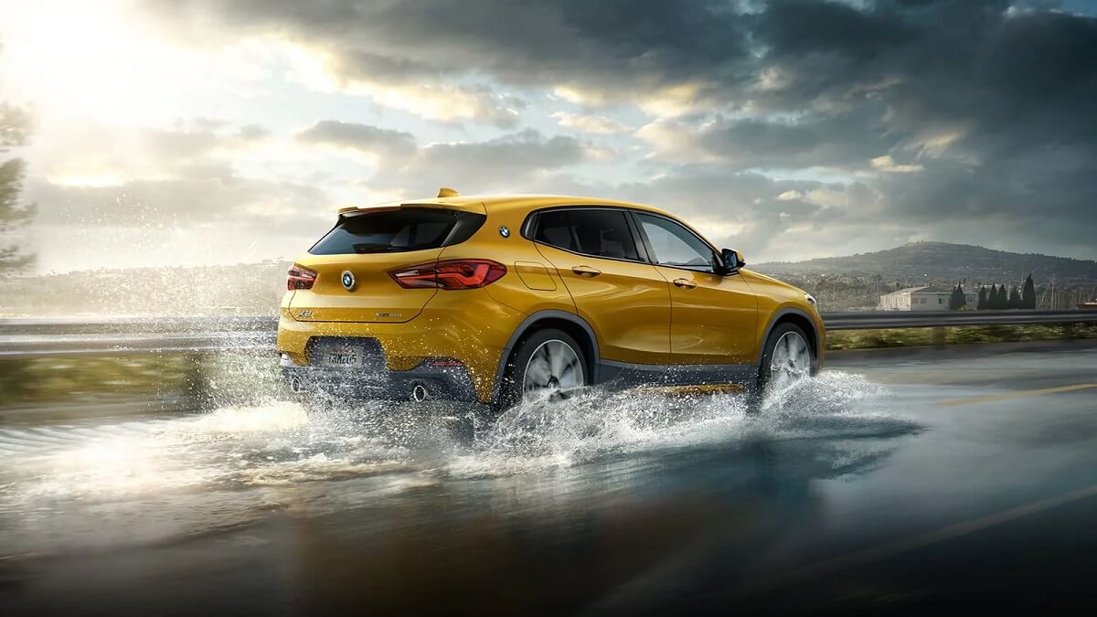 Traseira do BMW X2 2022 na cor amarela, andando sobre poça de água