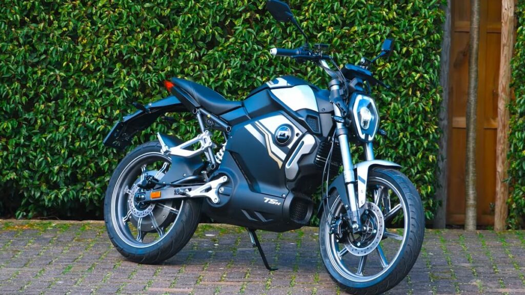 Super Soco TSX cinza em uma calçada com folhagens atrás
