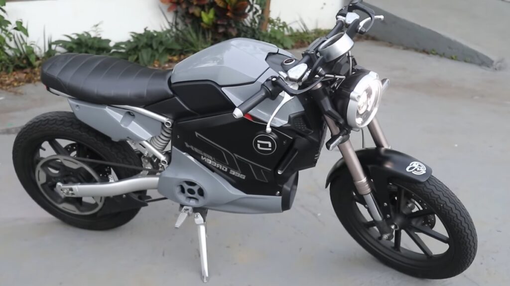 Super Soco TC Max em um estacionamento com plantas ao fundo.