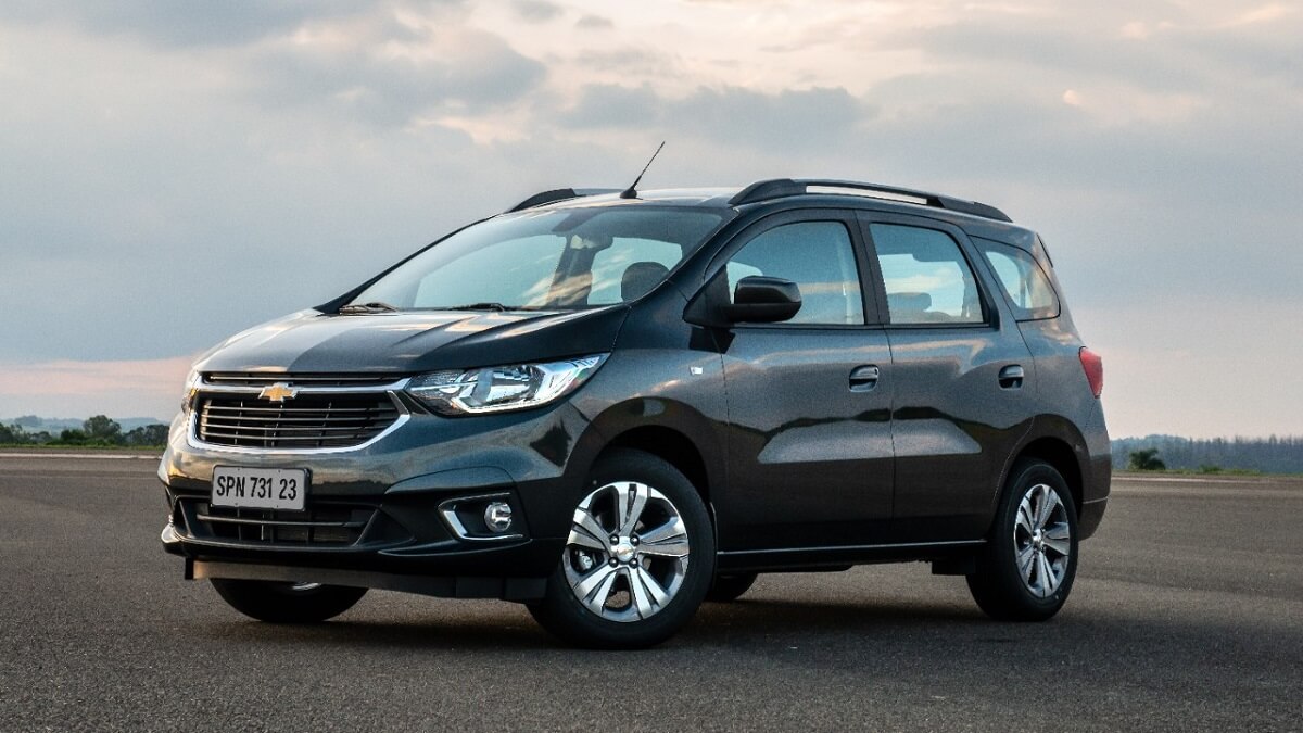 Lateral frontal de uma Chevrolet Spin 2023 na cor preta, em um asfalto com um céu nublado