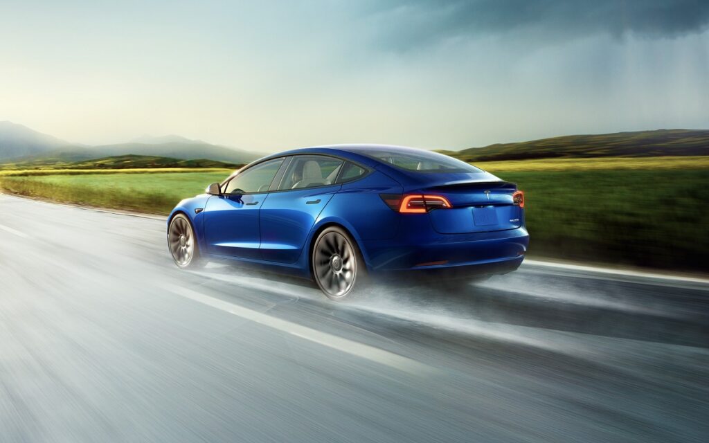 tesla modelo 3 na cor azul, com fundo de estrada em verde e cinza
