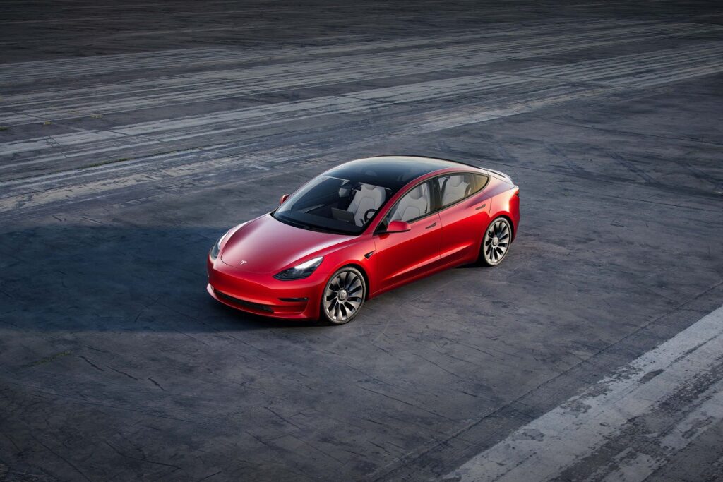 Carro da tesla modelo 3, na cor vermelha, e um fundo todo cinza