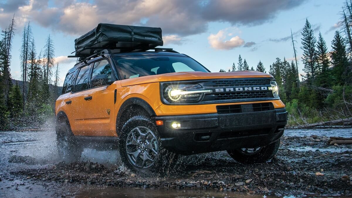 Lateral frontal de uma Ford Bronco 2023 na cor amarela, com partes em preto a beira de um riacho com o chão de pedras. Foto: divulgação
