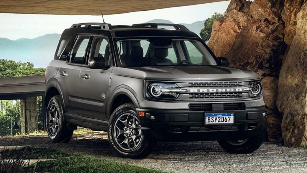 Lateral frontal de uma Ford Bronco 2023 na cor prata, com partes em preto estacionado em uma garagem com pedregulhos na lateral