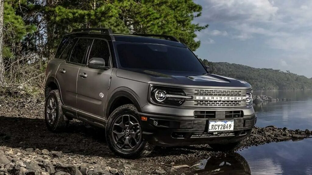Lateral frontal de uma Ford Bronco 2023 na cor prata estacionada em frente a um rio com árvores ao fundo
