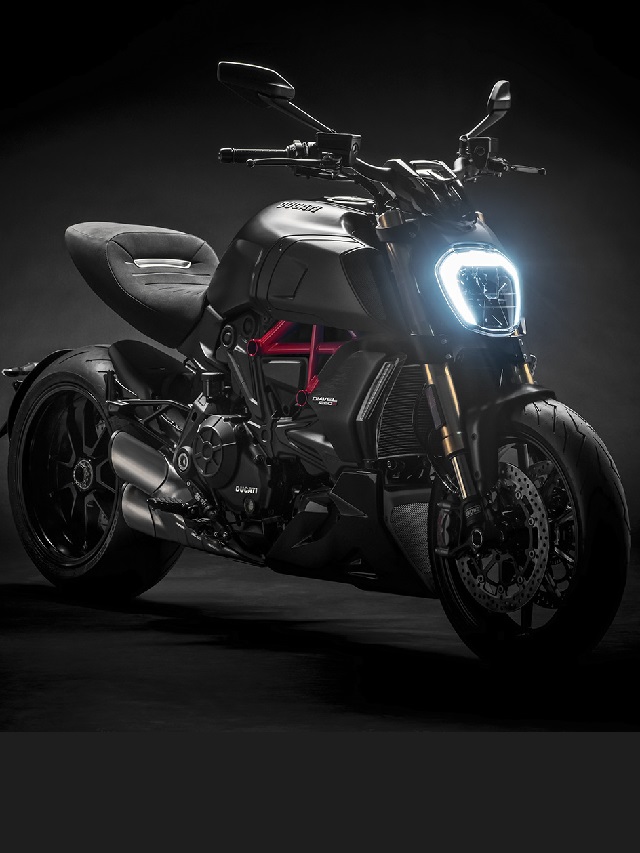 Lateral frontal de uma Ducati Diavel 1260 S 2022 preta com um detalhe lateral vermelho em um fundo preto com o farol ligado