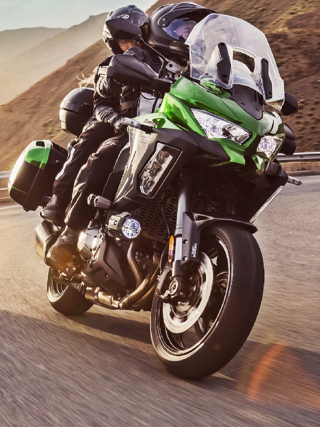 Lateral frontal de uma Versys 2022 verde com um casa rodando no asfalto ao por-do-sol