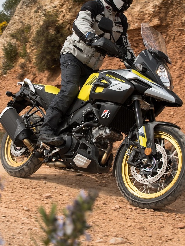 Lateral de uma Suzuki V-Strom 650 2022 amarela andando por um terreno de barro.