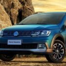 Lateral frontal de uma VW Saveiro 2023 na cor azul, estacionada em um chão de barro com uma paisagem montanhosa.