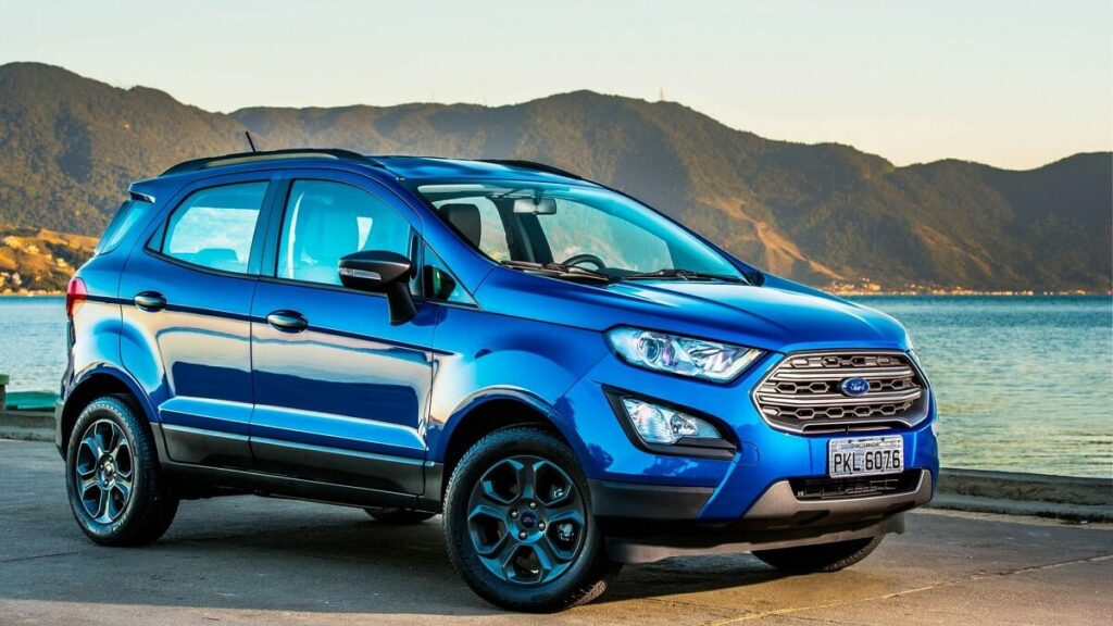 Lateral de uma Ford EcoSport 2023 na cor azul estacionado em um acostamento com o ar ao fundo.