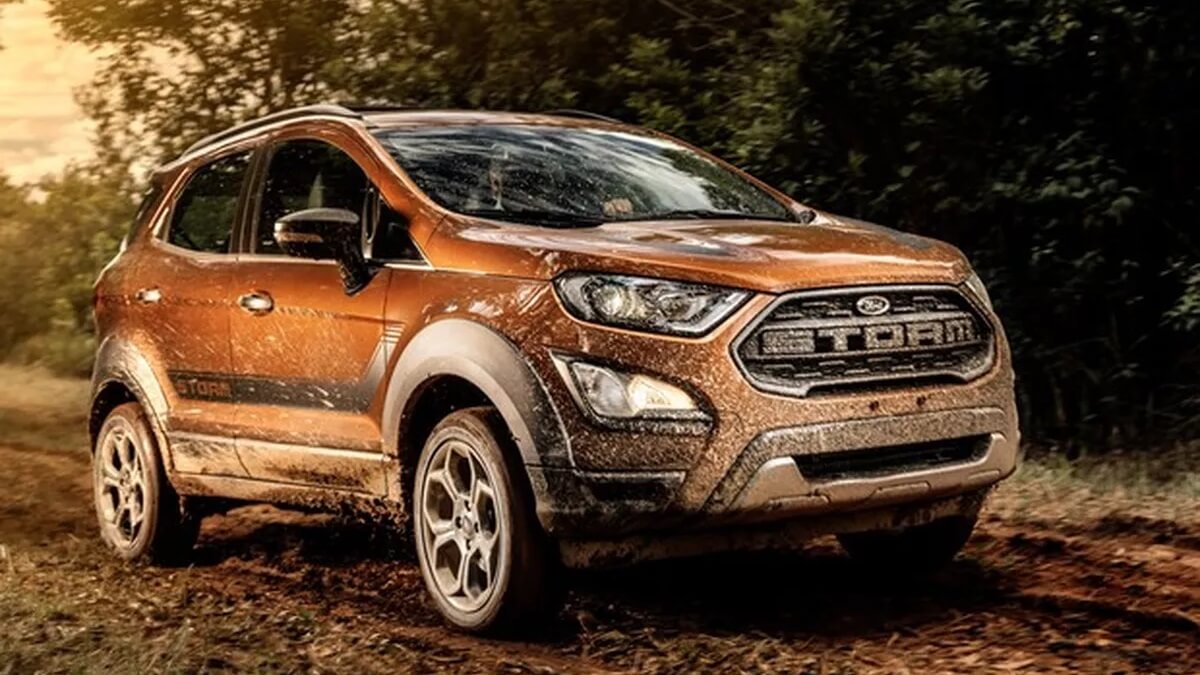 Lateral frontal de uma Ford EcoSport 2023 na cor laranja suja de lama rodando por um estrada lamacenta com vegetação ao fundo.