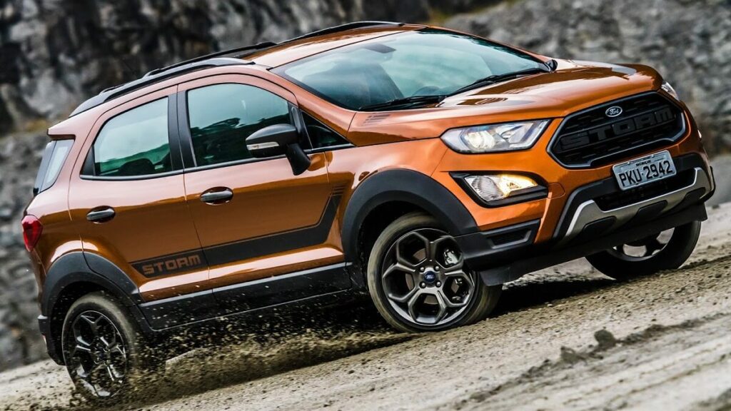 Lateral de um Ford EcoSport 2023 na cor laranja rodando por uma estrada de chão lamacenta.