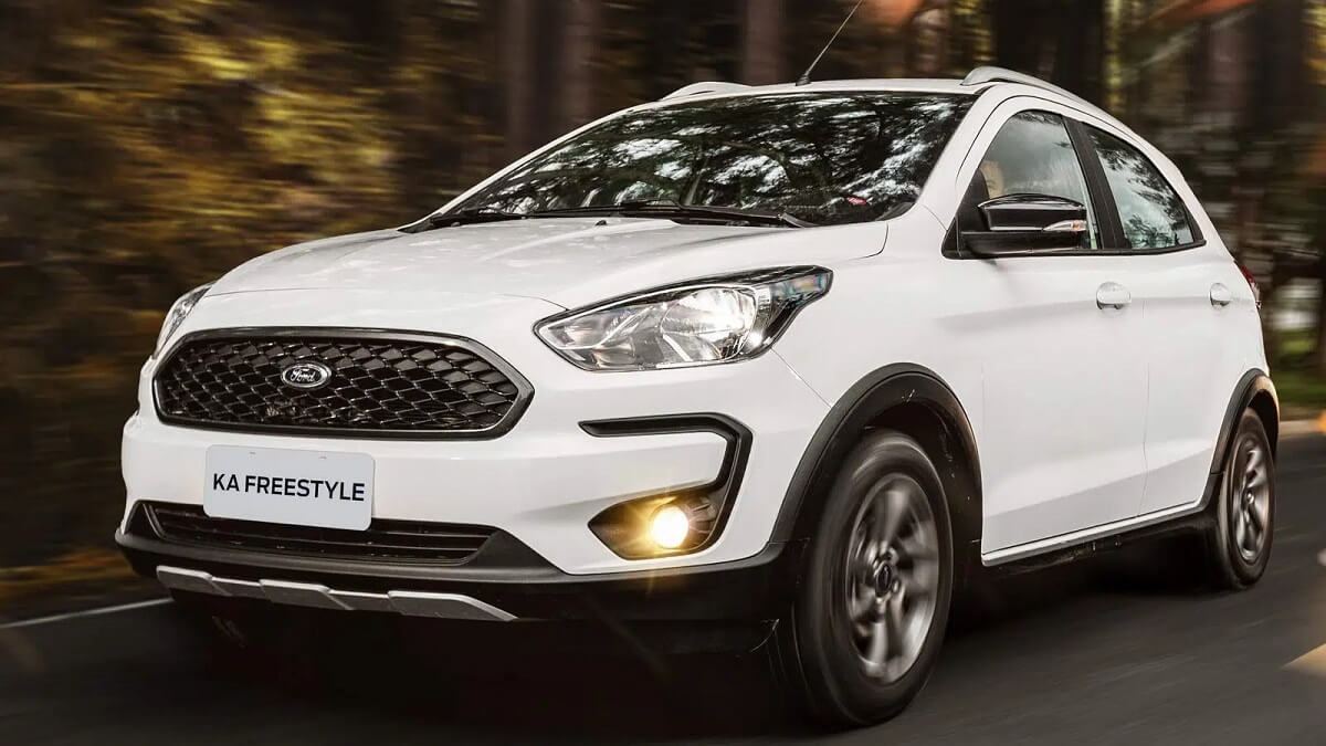Lateral frontal de uma Ford Ka 2023 na cor branca rodando por um estrada com vegetação ao fundo.