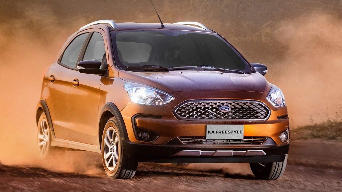 Lateral frontal de uma Ford Ka 2023 na cor laranja, suja e rodando por uma estrade barro