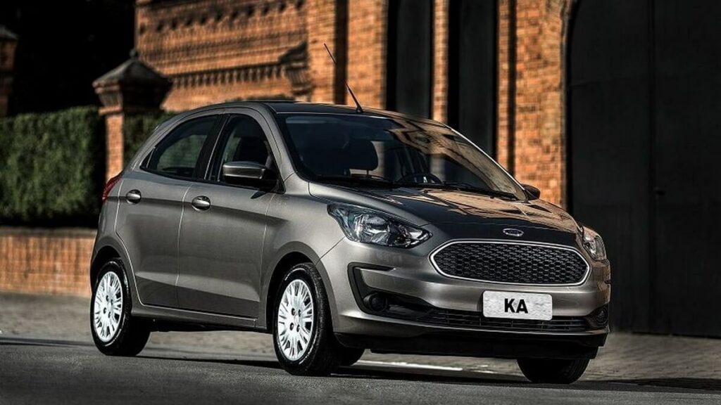 Lateral frontal de uma Ford Ka 2023 na cor preta rodando por uma estrada em meio a uma cidade