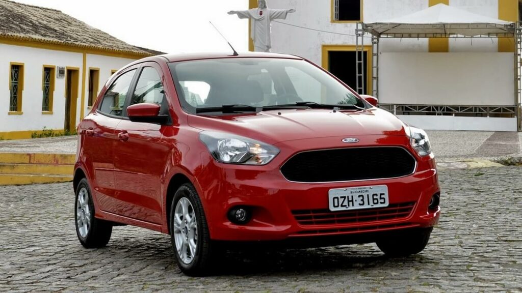 Lateral frontal de uma Ford Ka 2023 na cor vermelha com partes em preto estacionada em uma praça