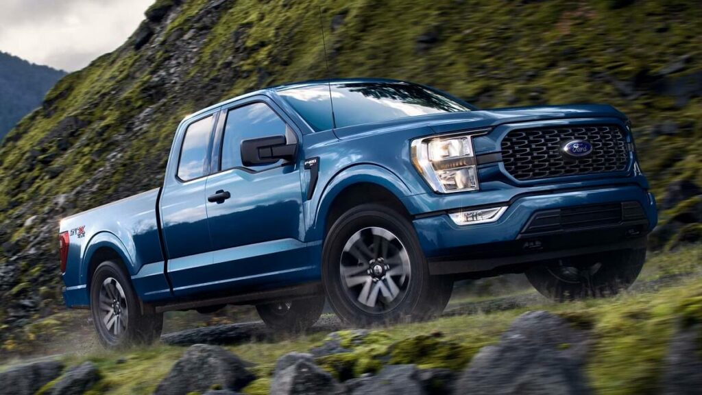 Lateral de uma Ford F-150 2023 na cor azul subindo por uma montanha rochosa