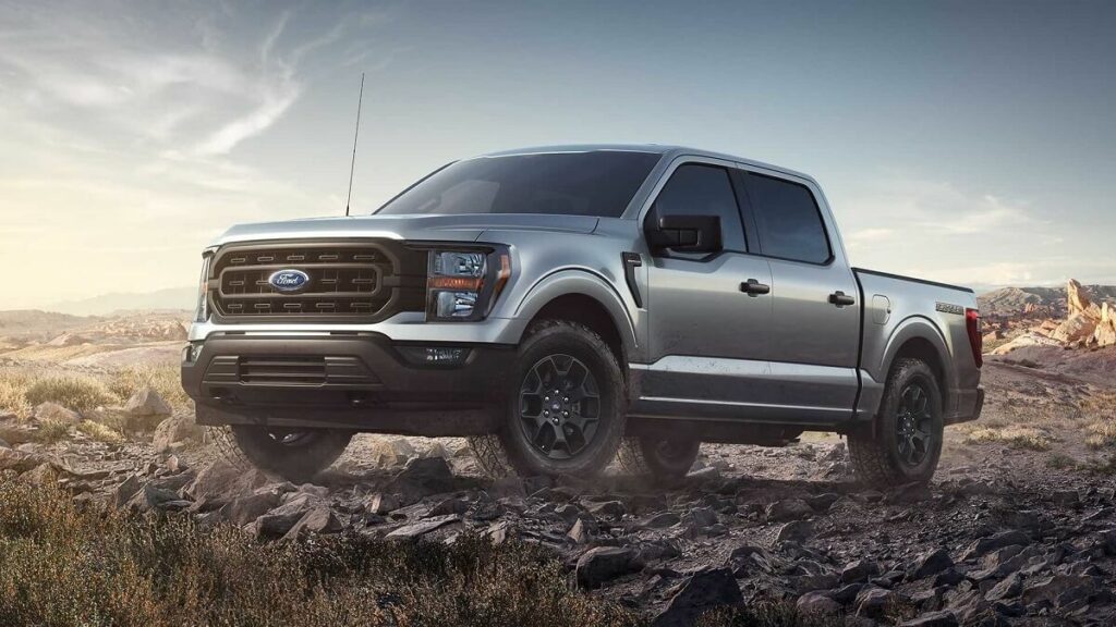 lateral frontal de uma Ford F-150 2023 na cor prata, estacionada em um chão de pedras.