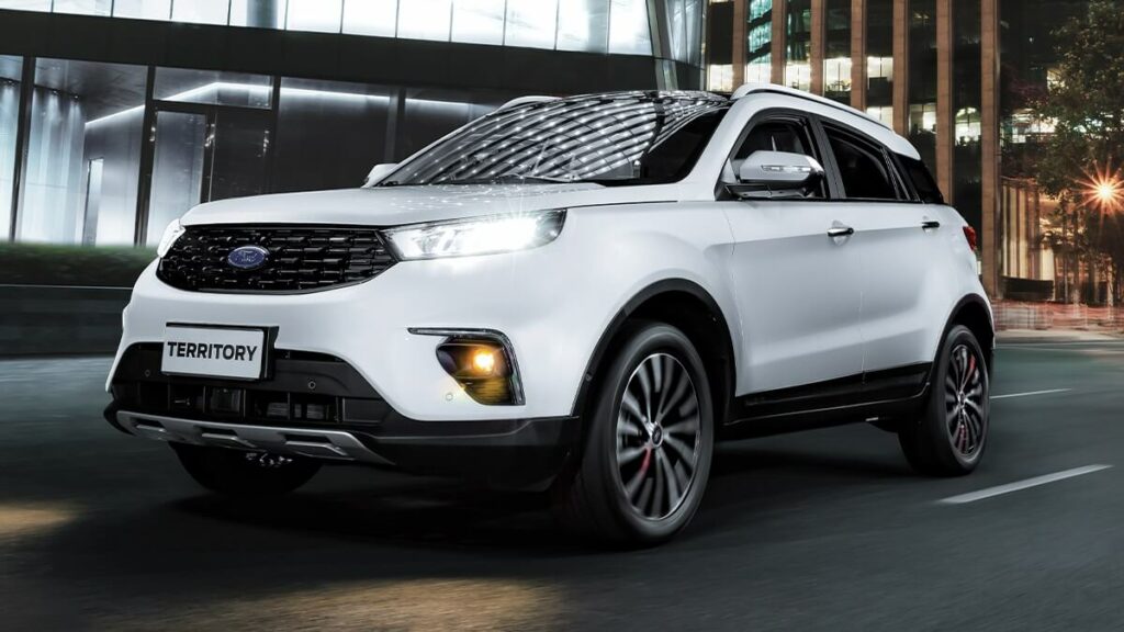 Lateral frontal de um Ford Territory 2023 na cor branca rodando por uma cidade no asfalto a noite.