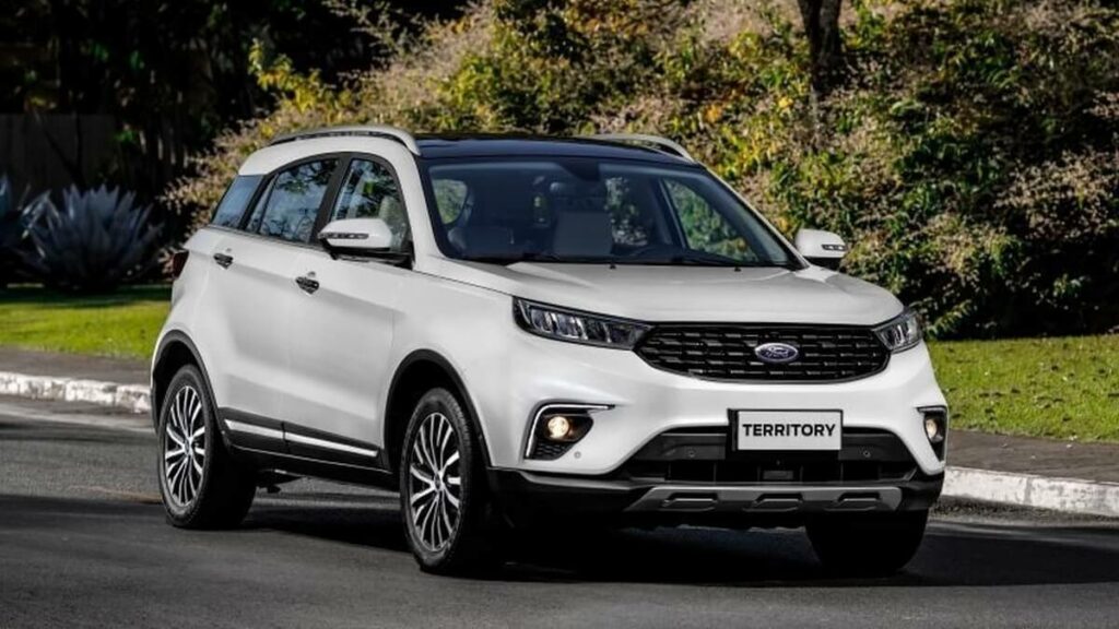 Lateral frontal de um Ford Territory 2023 na cor branca rodando por uma estrada na cidade com um gramado ao fundo.