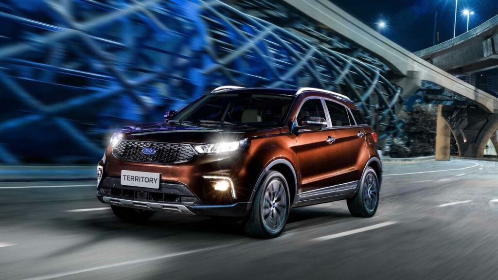 Lateral frontal de uma Ford Territory 2023 na cor laranja escura rodando por uma cidade a noite.