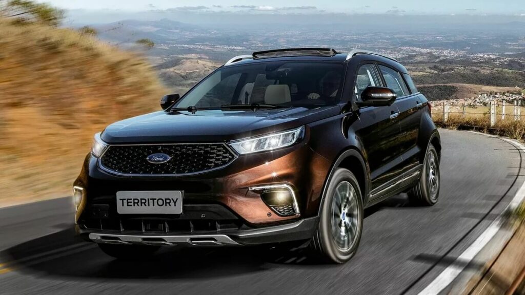 Lateral frontal de um Ford Territory 2023 na cor laranja escuro rodando no asfalto com montanhas ao fundo.