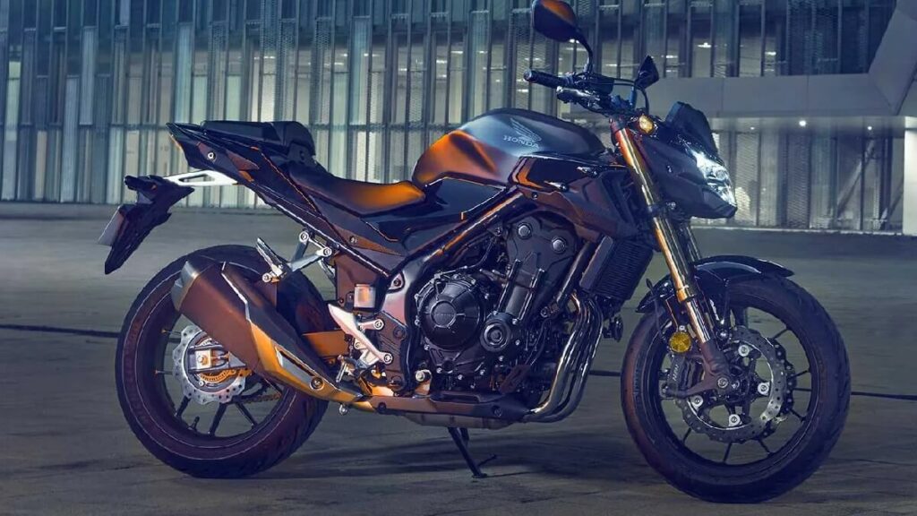 Lateral de uma CB 500F 2023 na cor preta, com partes douradas durante a noite em uma estrada.