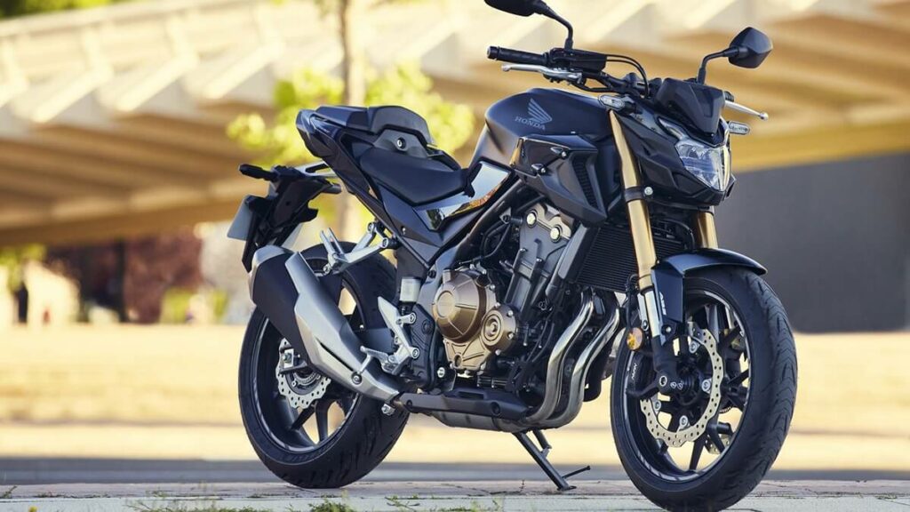 Lateral frontal de uma CB 500F 2023 na cor preta, com detalhes em dourado estacionada no asfalto