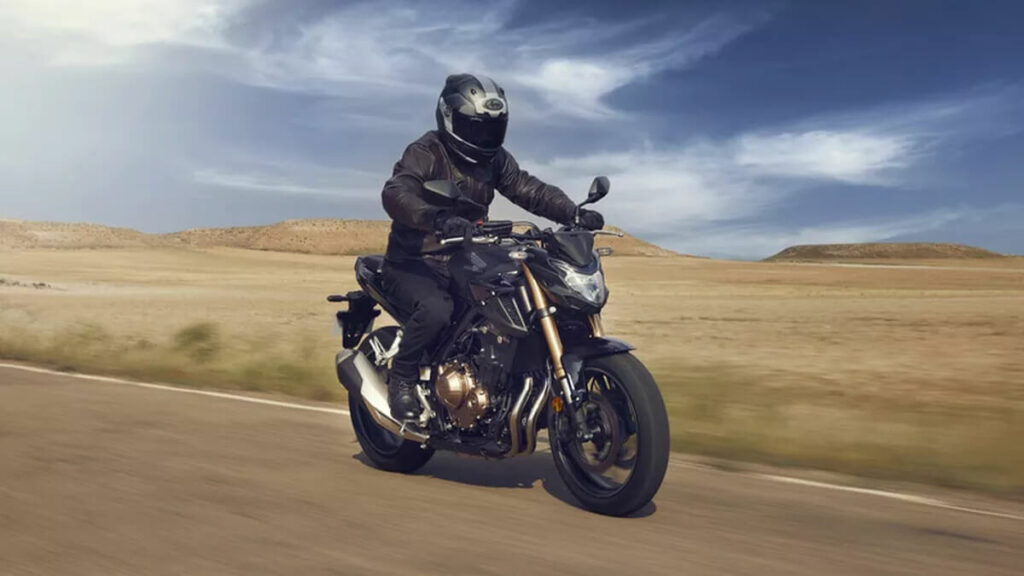 Lateral frontal de uma CB 500F 2023 na cor preta com detalhes em dourado rodando por uma estrada próximo a um deserto