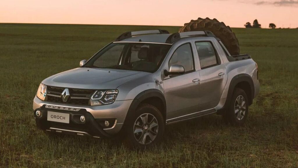 Lateral frontal Oroch 2023 em um campo com um pneu de trator na caçamba.