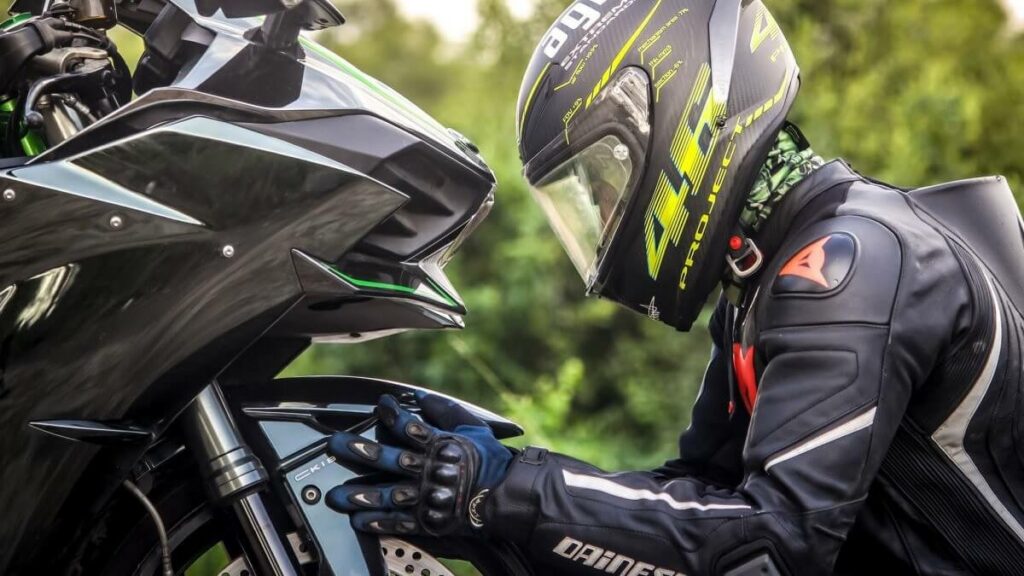 Motociclista abaixado em frente ao pneu dianteiro da moto