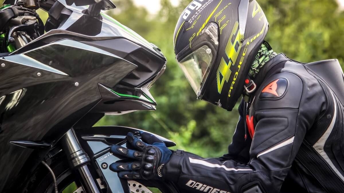 Motociclista abaixado em frente ao pneu dianteiro da moto