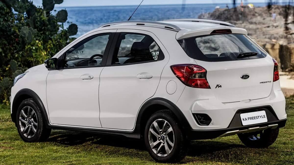 Lateral traseira Ford Ka 2023 na cor branca estacionada em um gramado com uma paisagem ao fundo