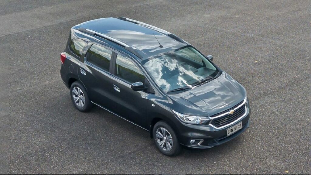 Lateral frontal com visão superior de uma Chevrolet Spin 2023 na cor preta estacionada em um asfalto.