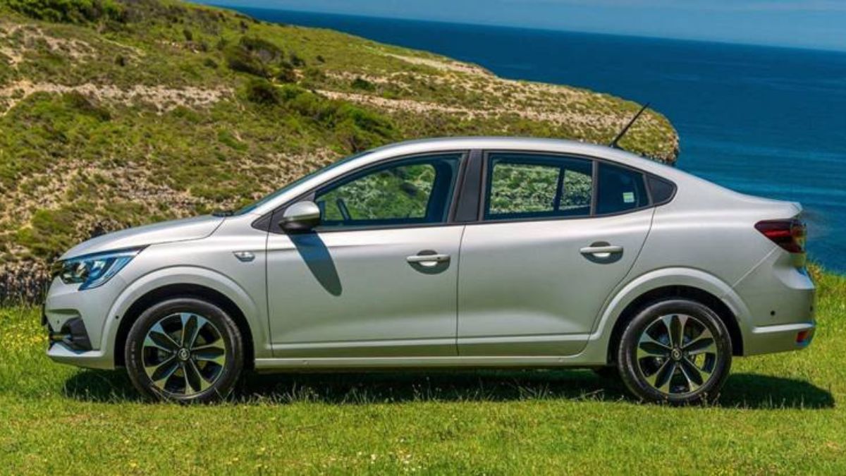 Lateral do Renault Logan 2023 prata, no alto de uma montanha com grama verde, com o mar ao fundo