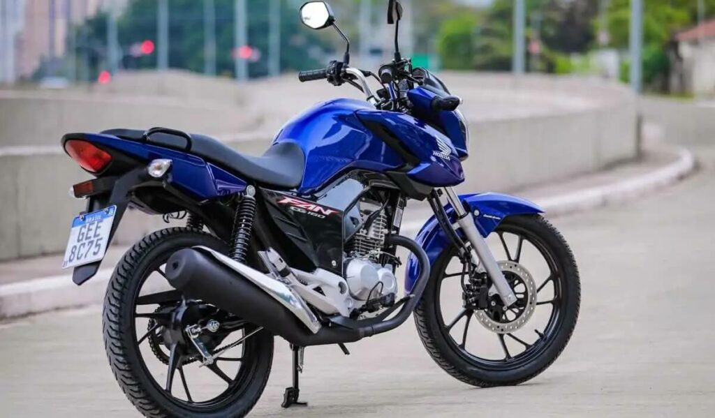 Foto lateral da Honda CG Fan 160 2023 a moto esta em uma estrada , moto na cor azul perolizado