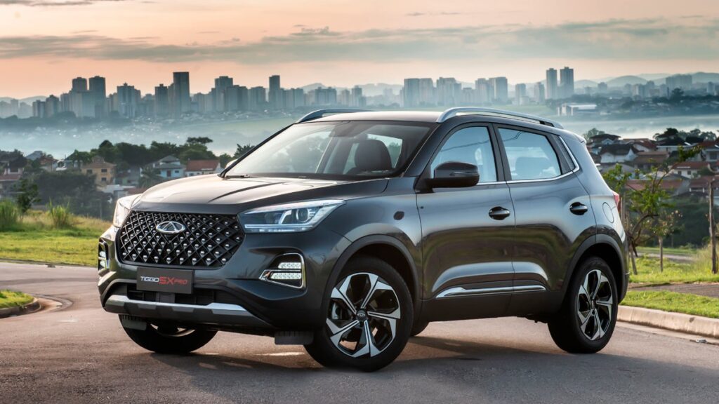 Foto do carro Tiggo 5X 2023, o carro esta estacionado na estrada e tem um por do sol no fundo da imagem