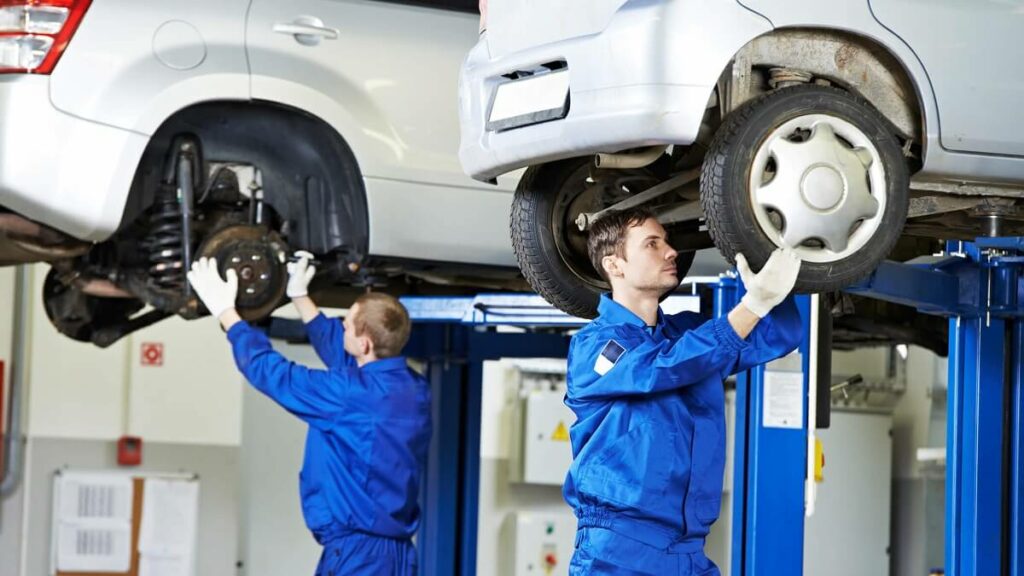 Dois mecânicos mexendo na roda de dois carros suspensos.