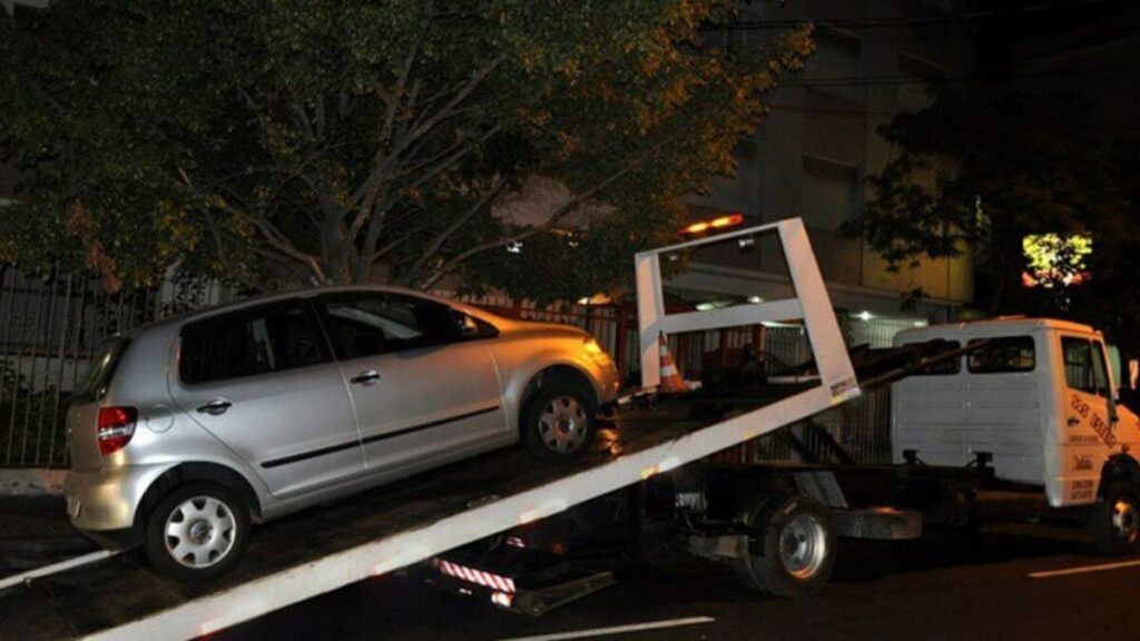 Carro branco sendo guinchado por conta de busca e apreensão de veículo