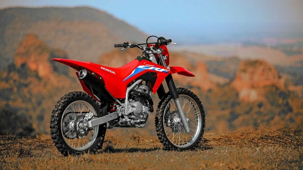 Foto traseira de uma Honda CRF 250 F 2023 vermelha estacionada em meio a uma mata baixa