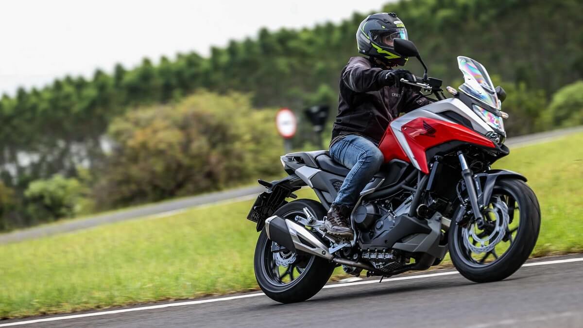 Foto lateral de uma pessoa andando com uma NC 750X 2023 vermelha