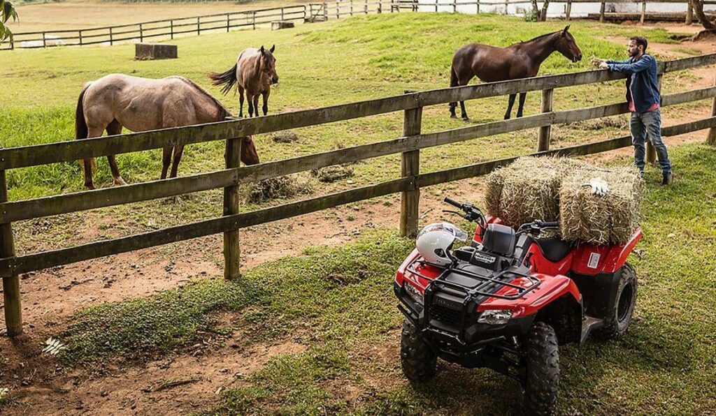 Foto de um TRX 420 Fourtrax 2023 vermelho puxando um fardo de feno