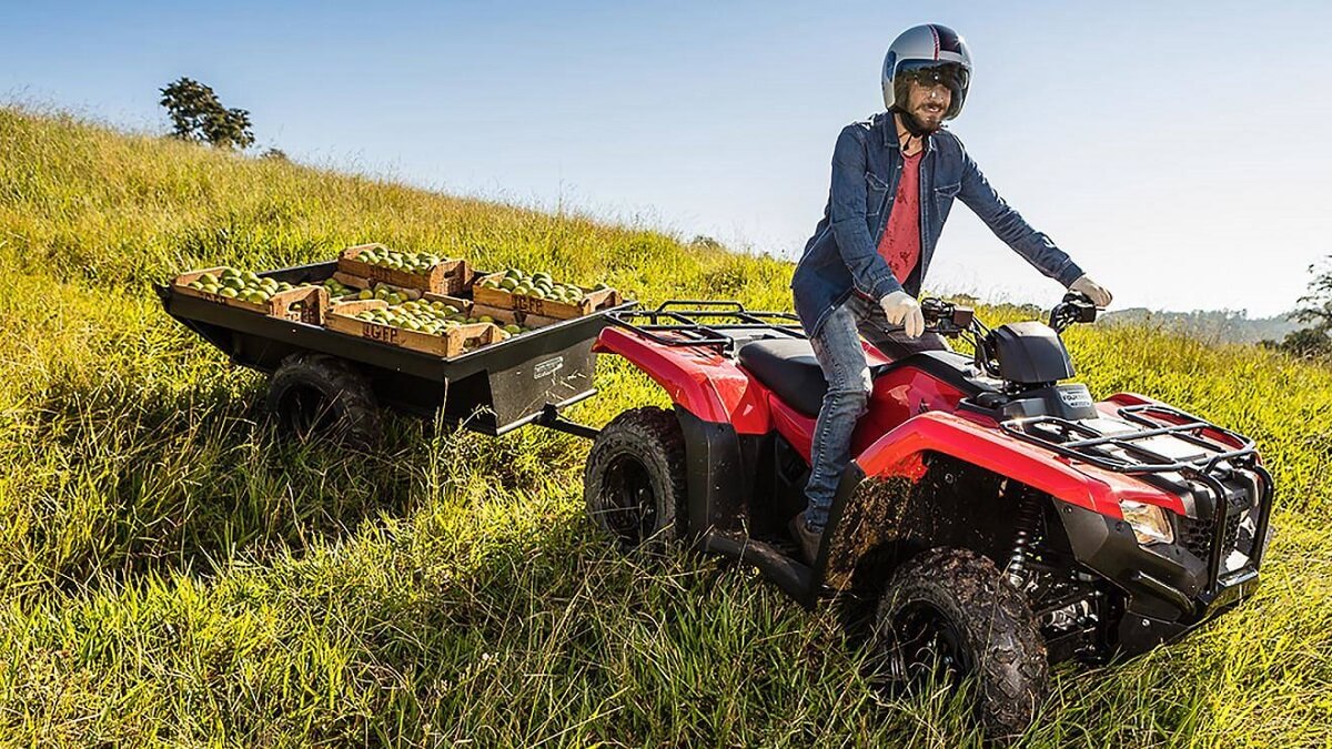 O quadriciclo TRX 420 Fourtrax 2023 está descendo um morro, e ele está puxando uma carretinha carregada