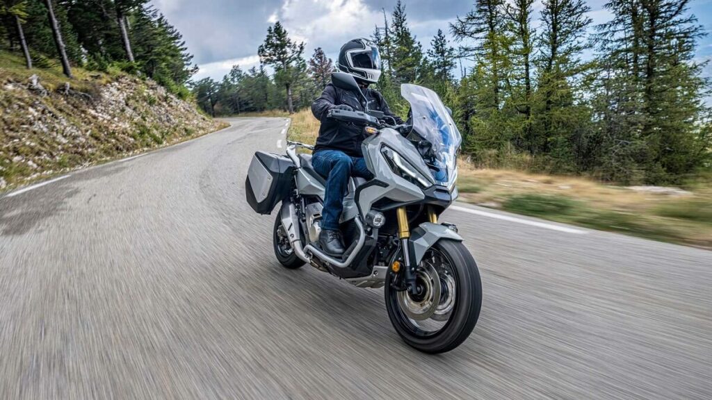 Foto de uma pessoa andando com uma X-ADV 2023 cinza em meio a uma floresta