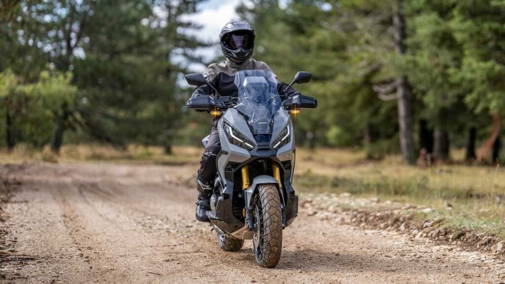 Foto de uma pessoa andando com uma X-ADV 2023 em uma estrada de chão