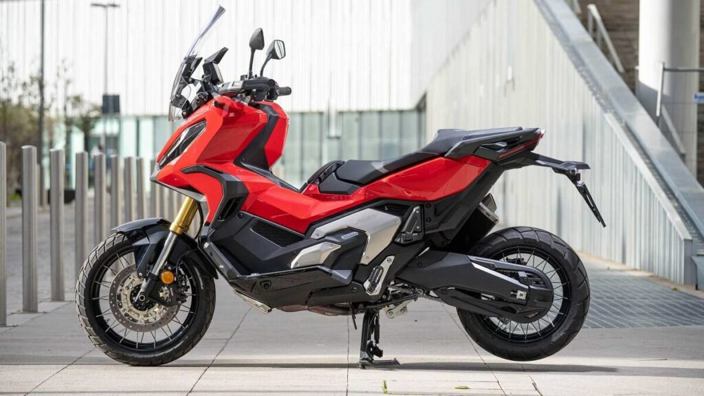 Foto lateral de uma X-ADV 2023 vermelha, a scooter está estacionada em uma espécie de entrada de garagem