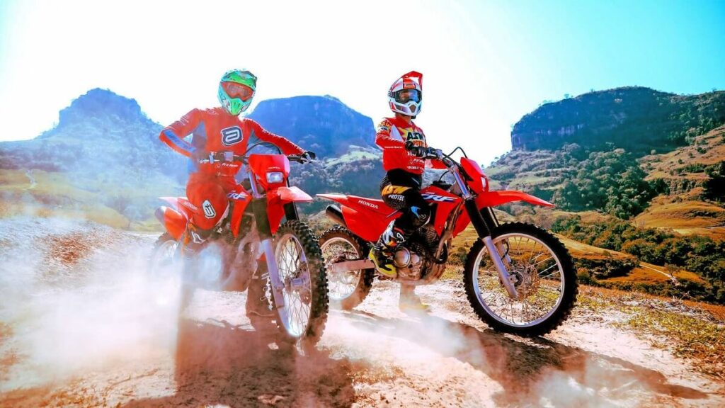 Duas pessoas andando de CRF 250 F 2023, na imagem cada pessoa está em cima de uma motocicleta, a cor da moto é vermelha e o traje dos motociclistas também são vermelhos