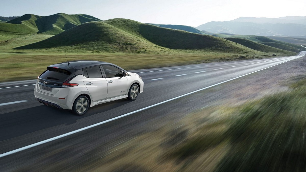 Foto de um Nissan Leaf 2023 andando em uma estrda que passa pelo meio de um campo aberto