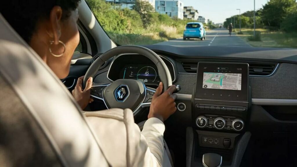 Foto do interior do carro, possui uma mulher dirigindo o veículo