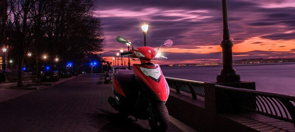 Foto de uma Lindy 125 2023 vermelha, atrás dela tem um por do sol